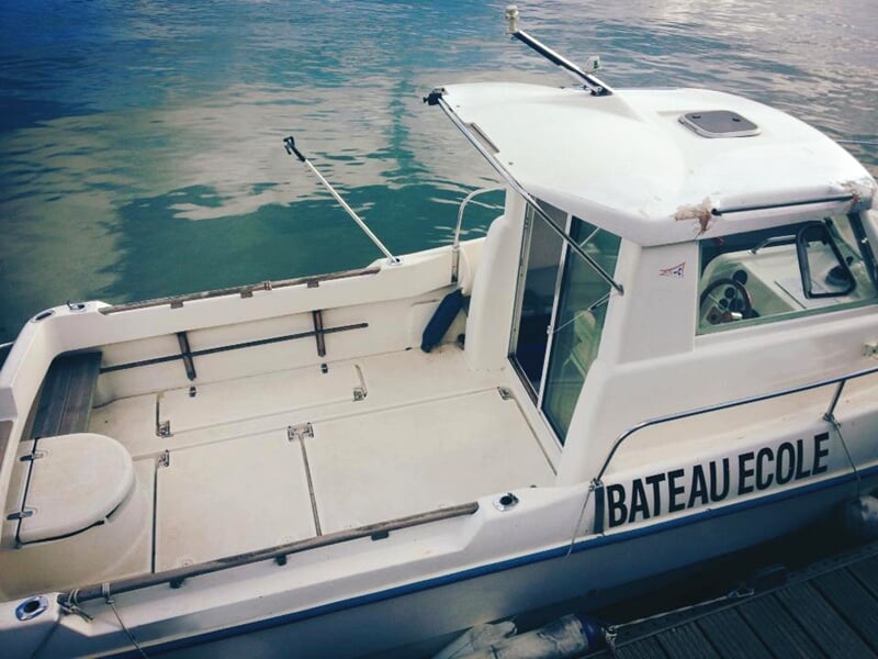 Bateau-école blanc amarré au quai, prêt pour la formation à la navigation avec un espace dégagé sur le pont arrière.