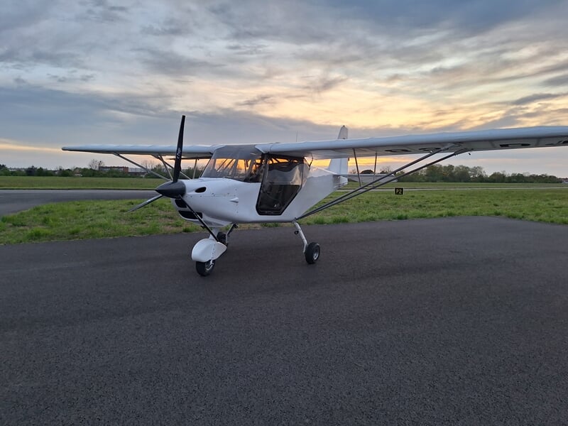 Petit ULM multiaxes blanc stationné sur une piste d'aérodrome au coucher du soleil avec ciel nuageux