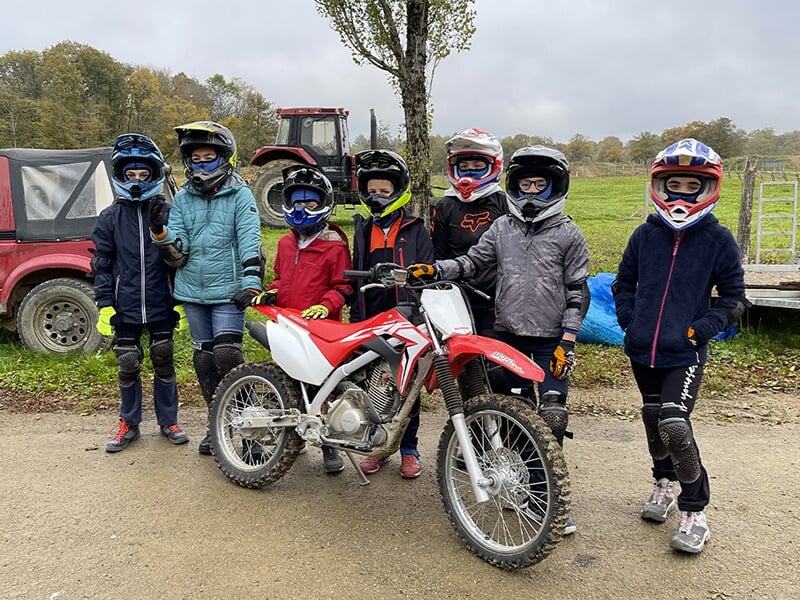 Groupe d'enfants en tenue complète de motocross, casques et protections, posant à côté d'une moto Honda CRF rouge et blanche.
