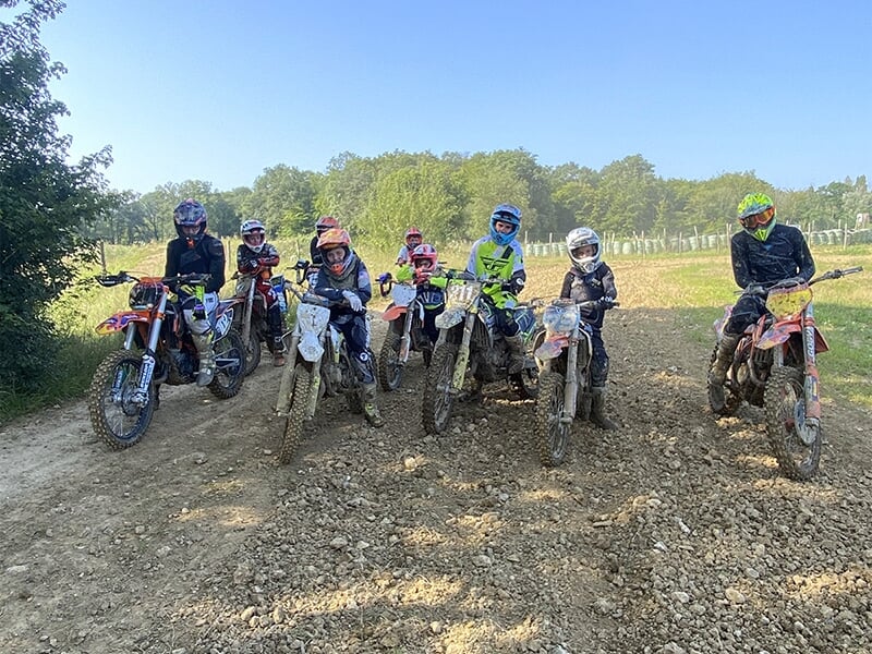 Groupe de jeunes motards en tenue de motocross, prêts à démarrer une course, alignés sur des motos tout-terrain.