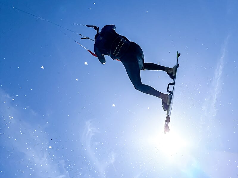 Kitesurfer en plein vol, avec une planche de kite jaune, sous un ciel bleu clair.