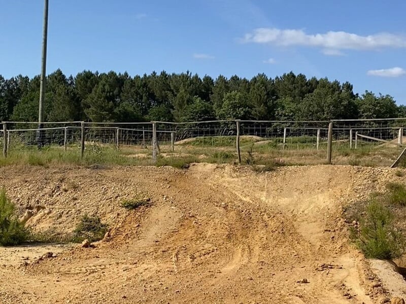 Vue d'une piste de motocross sèche et poussiéreuse avec quelques petites bosses, entourée de clôtures et de végétation.
