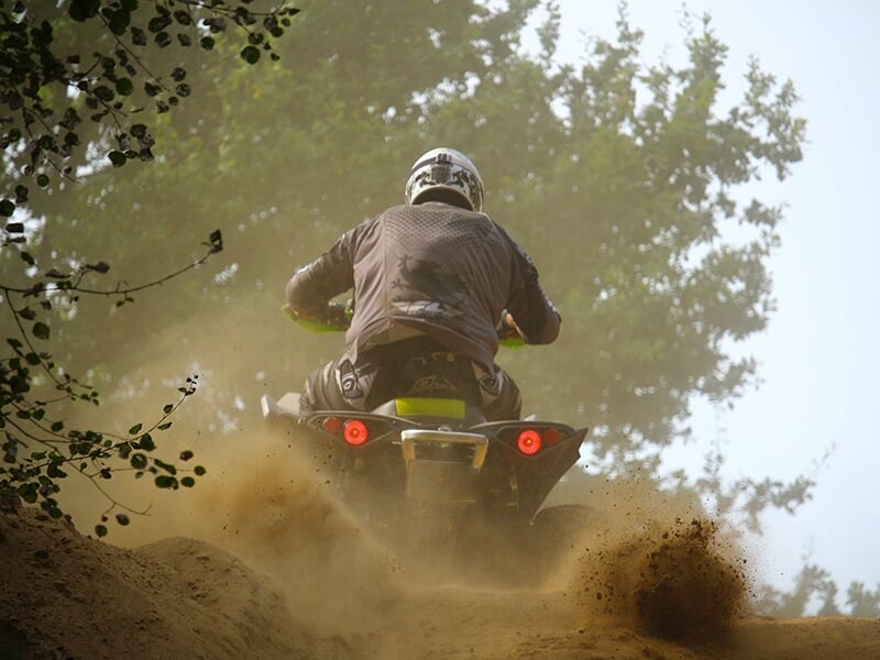 Quad en pleine accélération dans un terrain sablonneux, projetant de la poussière autour de lui.