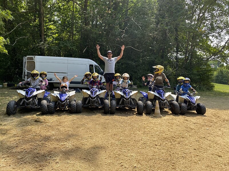 Groupe de jeunes pilotes sur des quads alignés pour une photo de groupe, accompagnés d'un adulte au centre les bras levés.