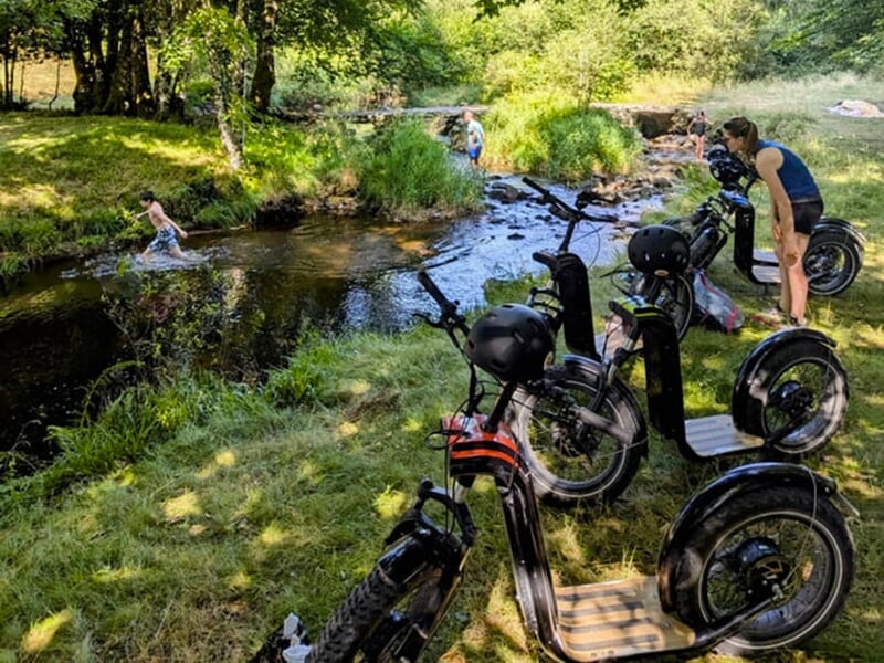 Un gros plan d'une trottinette électrique tout-terrain noire sur un sentier forestier, avec une personne dessus.