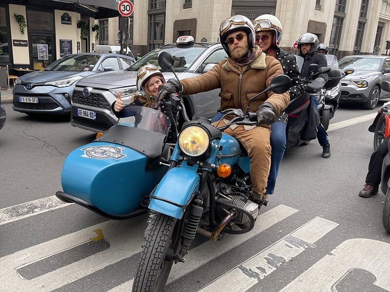 Un groupe de trois personnes en side-car vintage sur une rue animée de Paris.