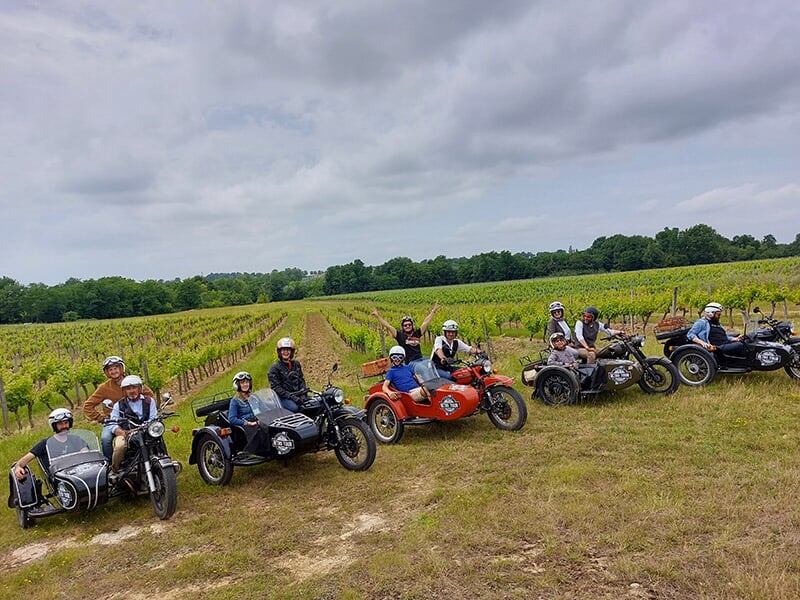 Un groupe de personnes en motos avec side-cars posant dans un grand vignoble.