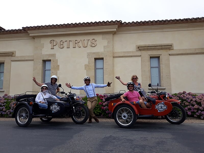 Deux motos avec side-cars devant le domaine Petrus avec les conducteurs et passagers posant joyeusement.