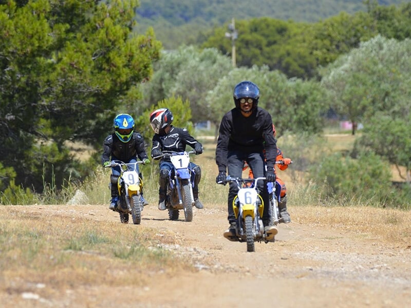 Groupe de jeunes motards sur un chemin de terre, suivi par un adulte en tête de file.