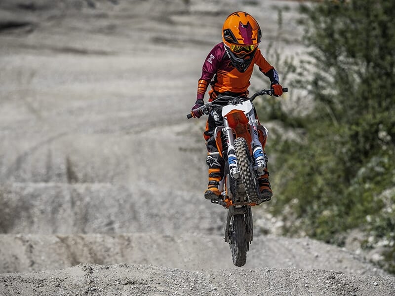 Motard en tenue orange sautant sur une bosse, concentré et en équilibre dans les airs.