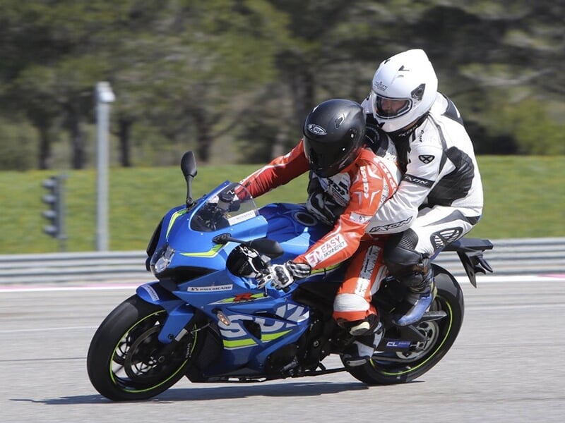 Motard en combinaison noire et passager en combinaison blanche sur une moto bleue