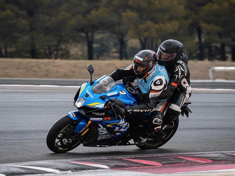 Duo de motards sur une moto de sport bleue en pleine vitesse sur circuit, en pleine inclinaison dans un virage.