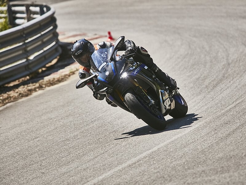Pilote sur une Yamaha R1 noire en pleine inclinaison, suivant la trajectoire d'un virage sur un circuit sécurisé par des barrières en métal.