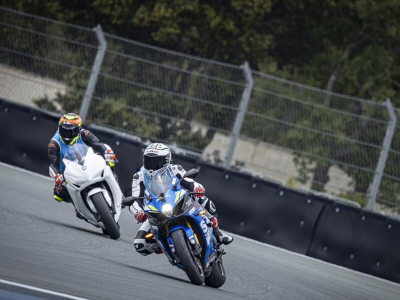 Deux motards en pleine course, portant des combinaisons de course et casques, l'un en bleu et l'autre en blanc, inclinés dans un virage.