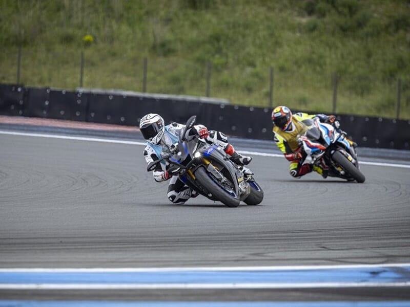 Deux motards en compétition sur un circuit, inclinaison extrême pour maintenir la trajectoire dans un virage.