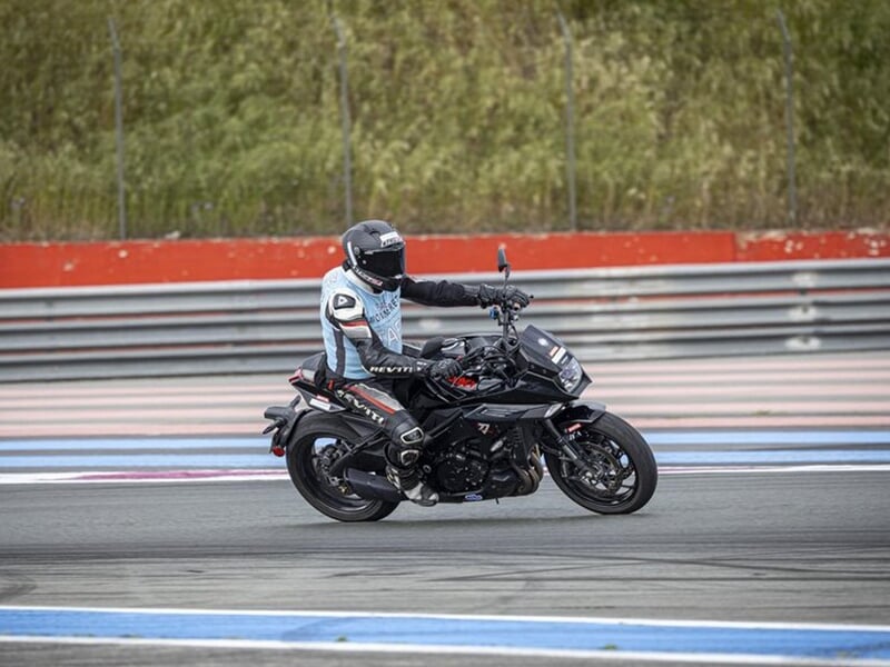 Motard portant un dossard bleu clair sur une moto noire, en mouvement lent sur la piste.