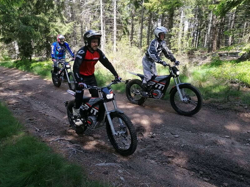 Trois personnes à moto sur chemin en forêt