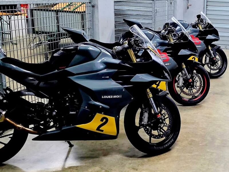 Quatre motos de course noires alignées dans un garage, avec des numéros jaunes et l'inscription