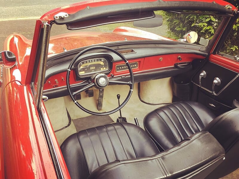 Intérieur d'une voiture décapotable rouge ancienne avec un tableau de bord rouge et noir, volant classique et sièges en cuir noir.