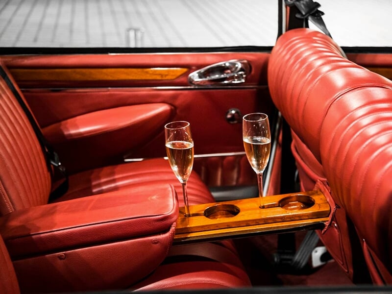 Intérieur de voiture de luxe avec sièges en cuir rouge et table en bois avec deux verres de champagne.