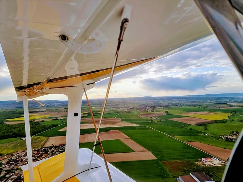 Vue depuis l'aile d'un avion en vol, surplombant un paysage rural avec champs et collines sous un ciel partiellement nuageux.