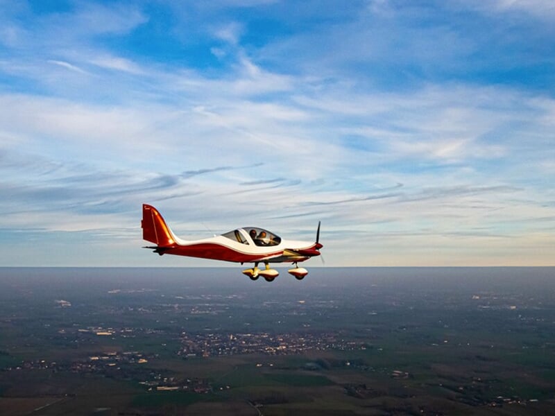 Vue d'un avion léger volant au-dessus d'une campagne sous un ciel dégagé avec des nuages légers.