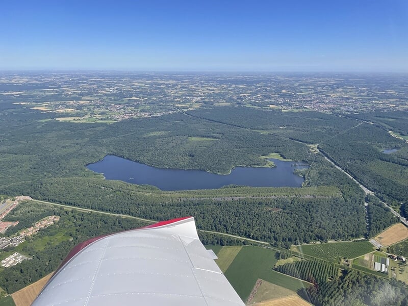 Vue aérienne d'un lac entouré de forêts et de champs, prise depuis l'aile d'un avion.