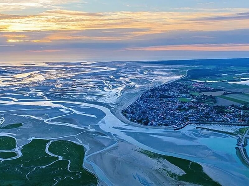 Vue aérienne spectaculaire d'une baie avec des bancs de sable, des cours d'eau sinueux et un coucher de soleil.