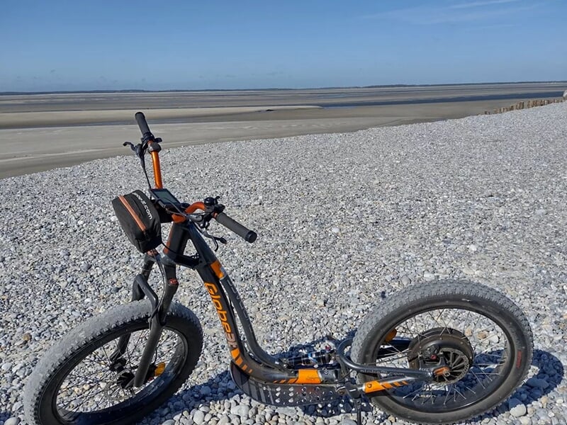 Trottinette électrique tout-terrain stationnée sur une plage de galets avec vue sur l’horizon marin.