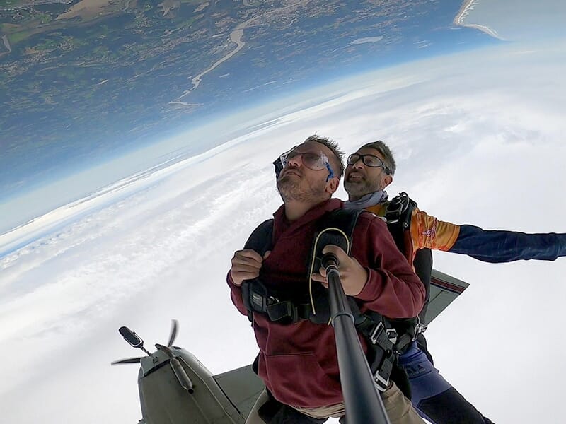 Deux parachutistes juste après avoir sauté de l’avion, avec une vue inversée sur le paysage terrestre.
