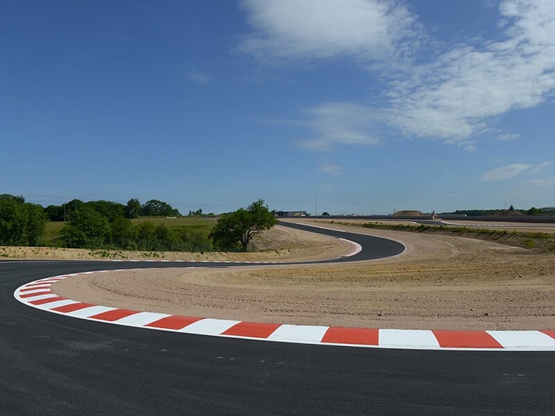 Courbe sinueuse d'une piste de course entourée de végétation et de terre.