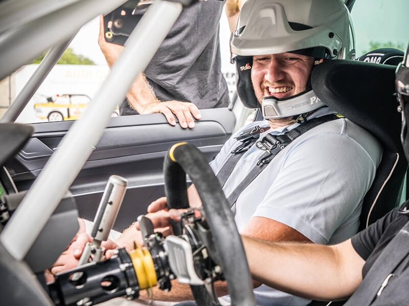 Personne souriante portant un casque dans une voiture de course.