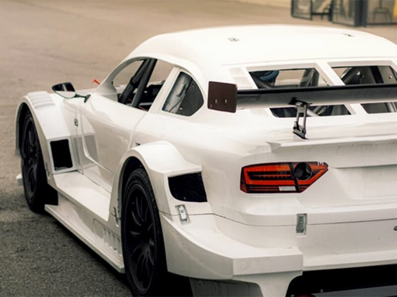 Vue arrière d'une voiture de course blanche avec un aileron et des détails aérodynamiques.