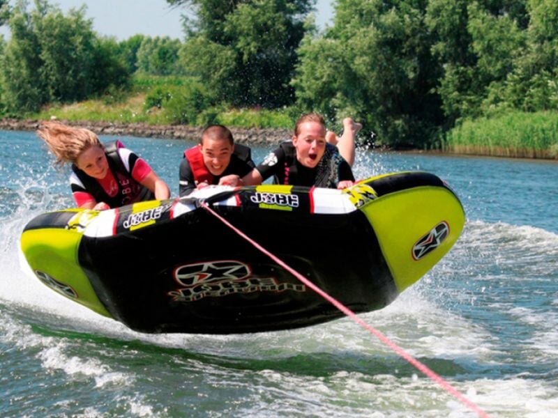 Trois personnes souriantes sur un gros bouée gonflable jaune tirée par un bateau sur un lac.