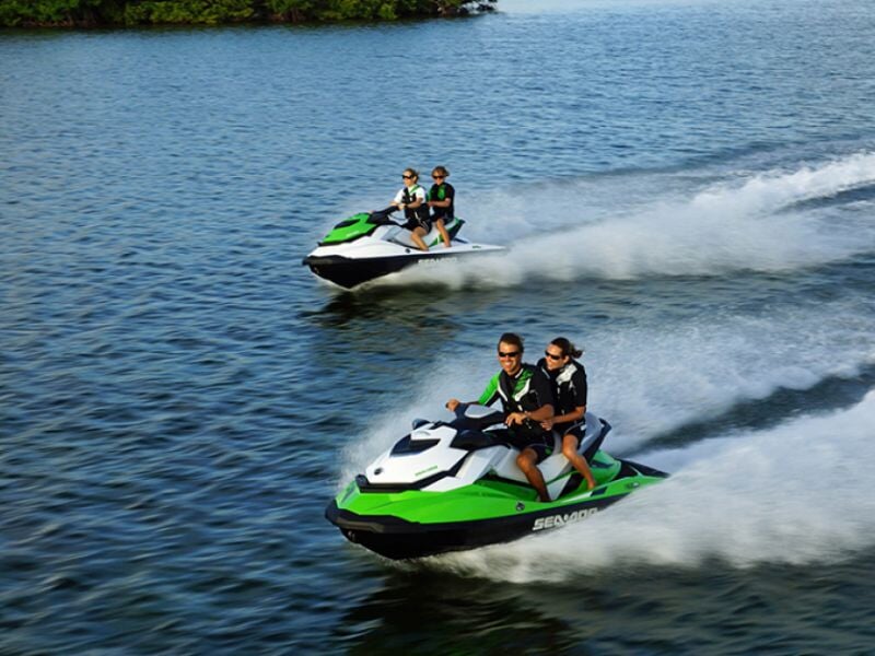 Deux jetskis verts et blancs avec des passagers roulant rapidement sur l'eau calme d'un lac.
