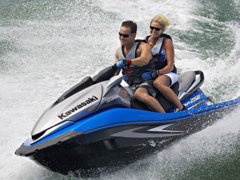 Couple en gilets de sauvetage sur un jetski Kawasaki bleu et blanc en train de naviguer sur l'eau.