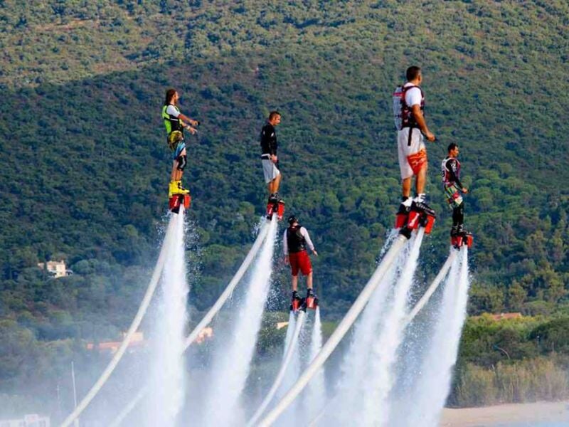 Groupe de personnes en flyboards sur un lac, propulsés par jets d'eau, avec des collines en arrière-plan.