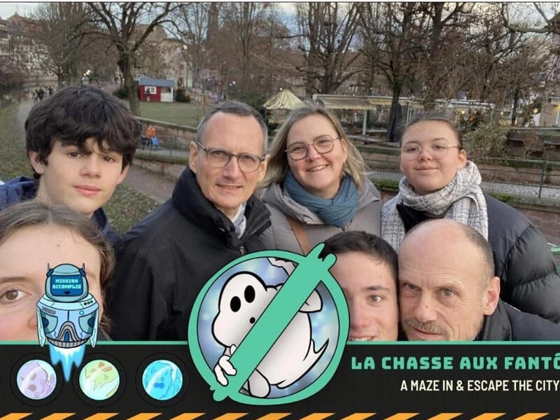 Famille souriante participant au jeu 'La Chasse aux Fantômes' avec les canaux et maisons typiques de Strasbourg en arrière-plan