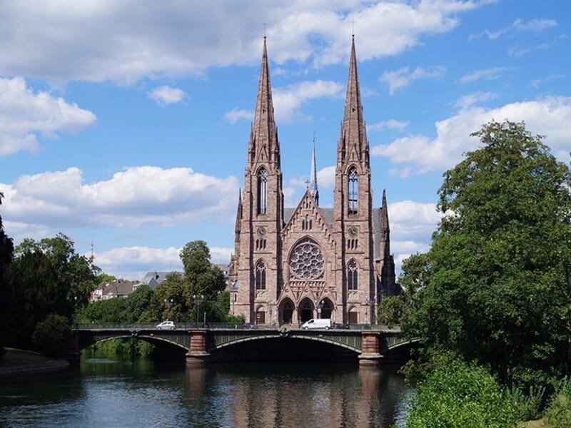 Vue de la façade gothique de l'église Saint-Paul de Strasbourg avec ses deux flèches, surplombant une rivière et un pont