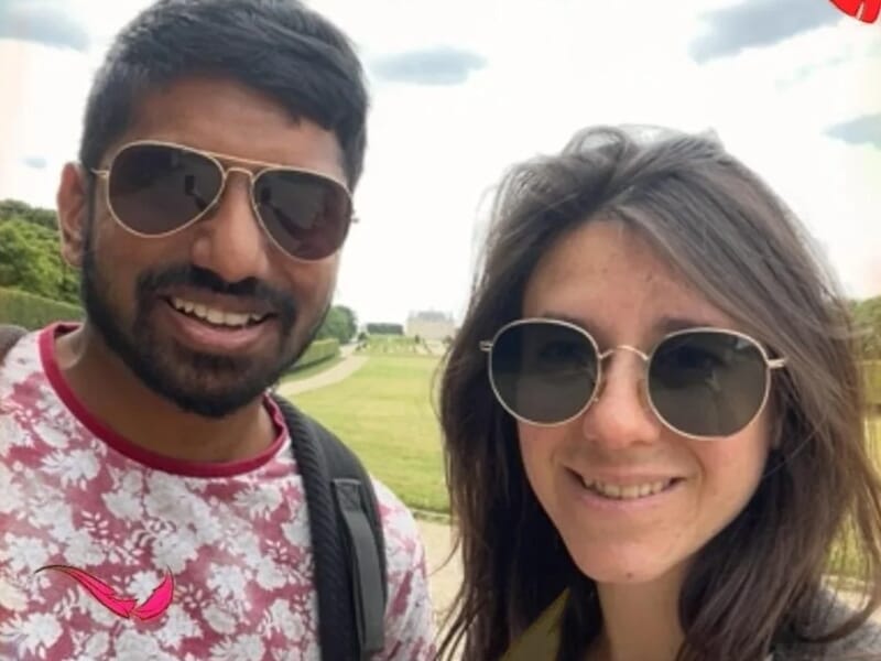 Selfie d’un couple souriant portant des lunettes de soleil, dans un parc avec une allée en perspective et des motifs de feuilles colorées autour de l’image