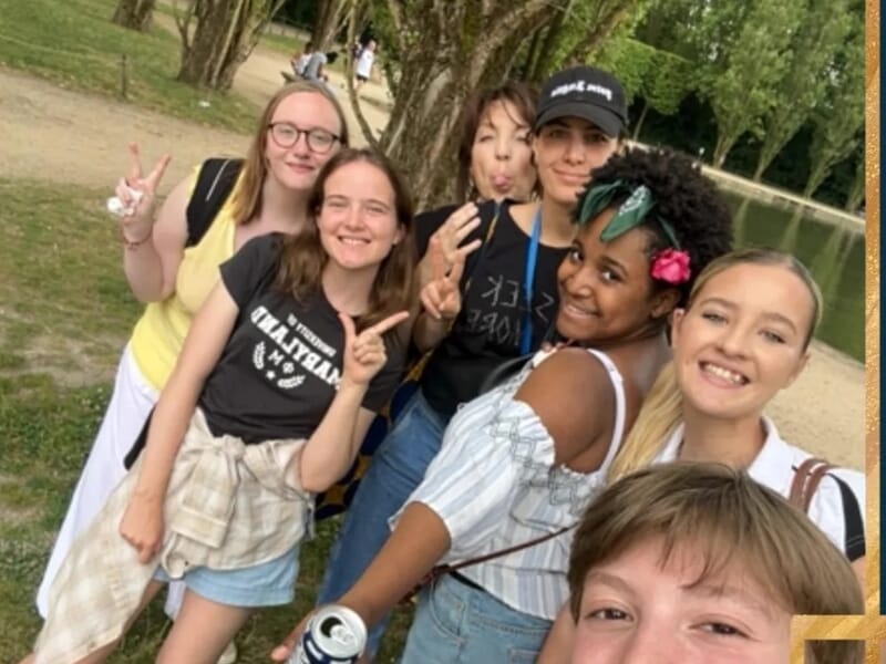 Groupe de jeunes femmes souriantes posant dans un parc boisé près d’un plan d’eau.