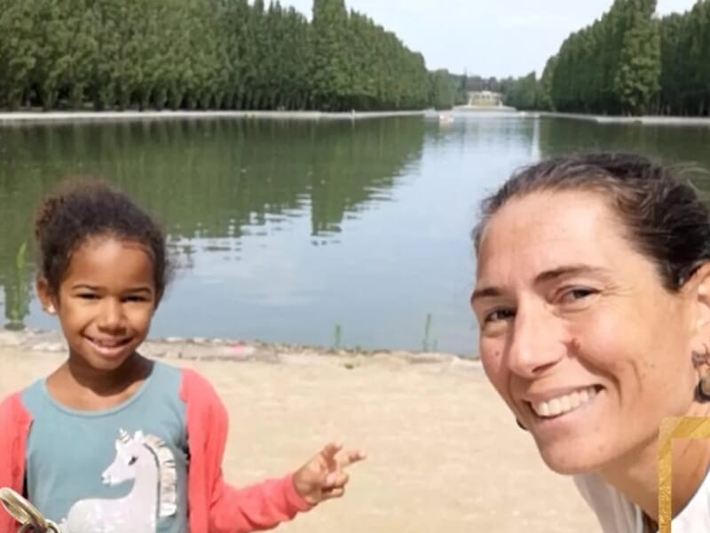 Selfie d'une femme et d'une fillette souriantes près d’un grand bassin entouré d’arbres.