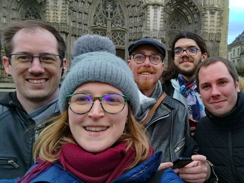 Groupe de cinq personnes souriantes posant devant une cathédrale gothique avec des détails sculptés.