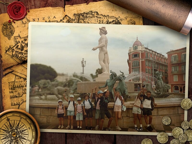 Groupe d'enfants posant joyeusement devant la Fontaine du Soleil à Nice, avec la statue d’Apollon et des figures en bronze, entourée de bâtiments rouges à volets verts et d’un ciel nuageux.