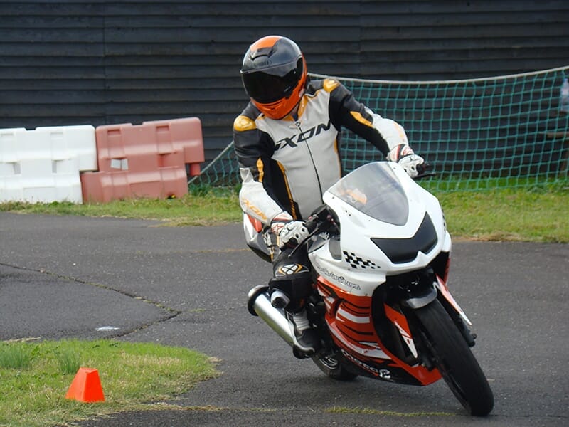 Motard penché sur un virage serré avec une combinaison et un casque, sur une petite piste.