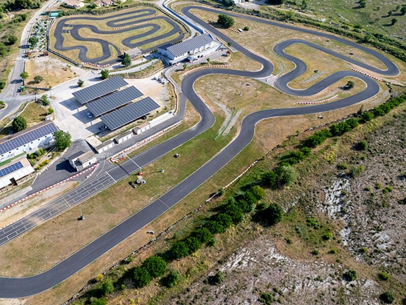 Vue aérienne d'un circuit complexe avec des tracés sinueux et des bâtiments équipés de panneaux solaires.