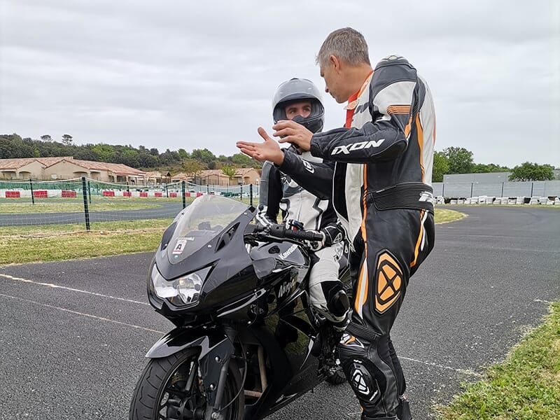 Instructeur discutant avec un motard assis sur une moto noire sur une piste de karting.