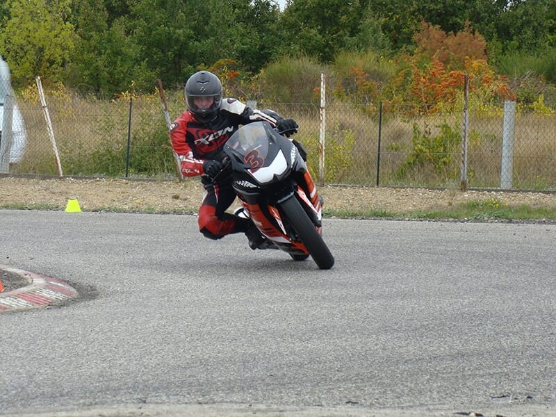 Motard en combinaison rouge prenant un virage incliné sur une moto de course sur un circuit.