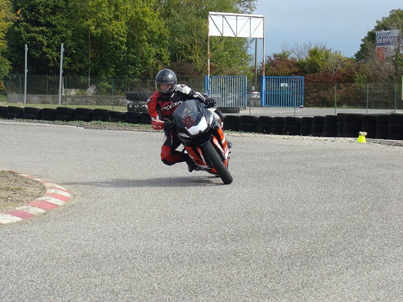 Motard en combinaison rouge et casque noir prenant un virage serré sur un circuit lors d'un stage de pilotage de moto sur circuit