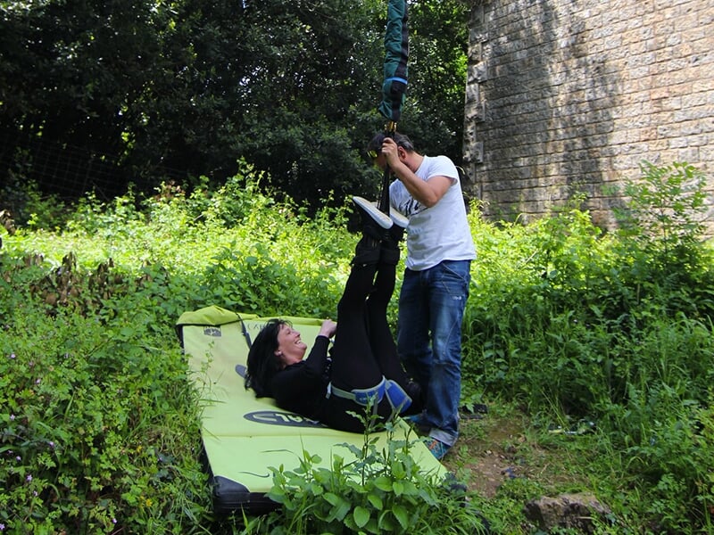 Personne allongée sur un matelas de réception après un saut à l'élastique, aidée par un membre de l'équipe pour se détacher.